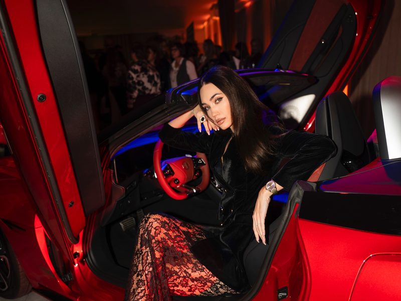 Dubravka Švegar in a black outfit with lace trousers, at the wheel of a red car